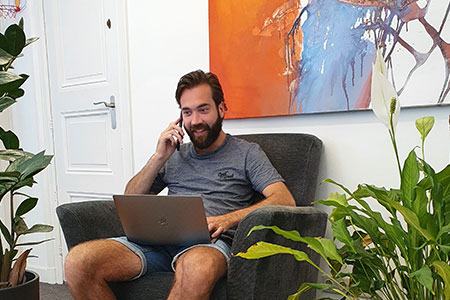 Scrumble medewerker die lachend aan het telefoneren is met een laptop op zijn schoot op een fauteuil