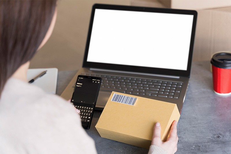 Beeld van een laptop, pakket en vrouw die levering verwerkt op haar telefoon - Digitalisering van Orderpicking.